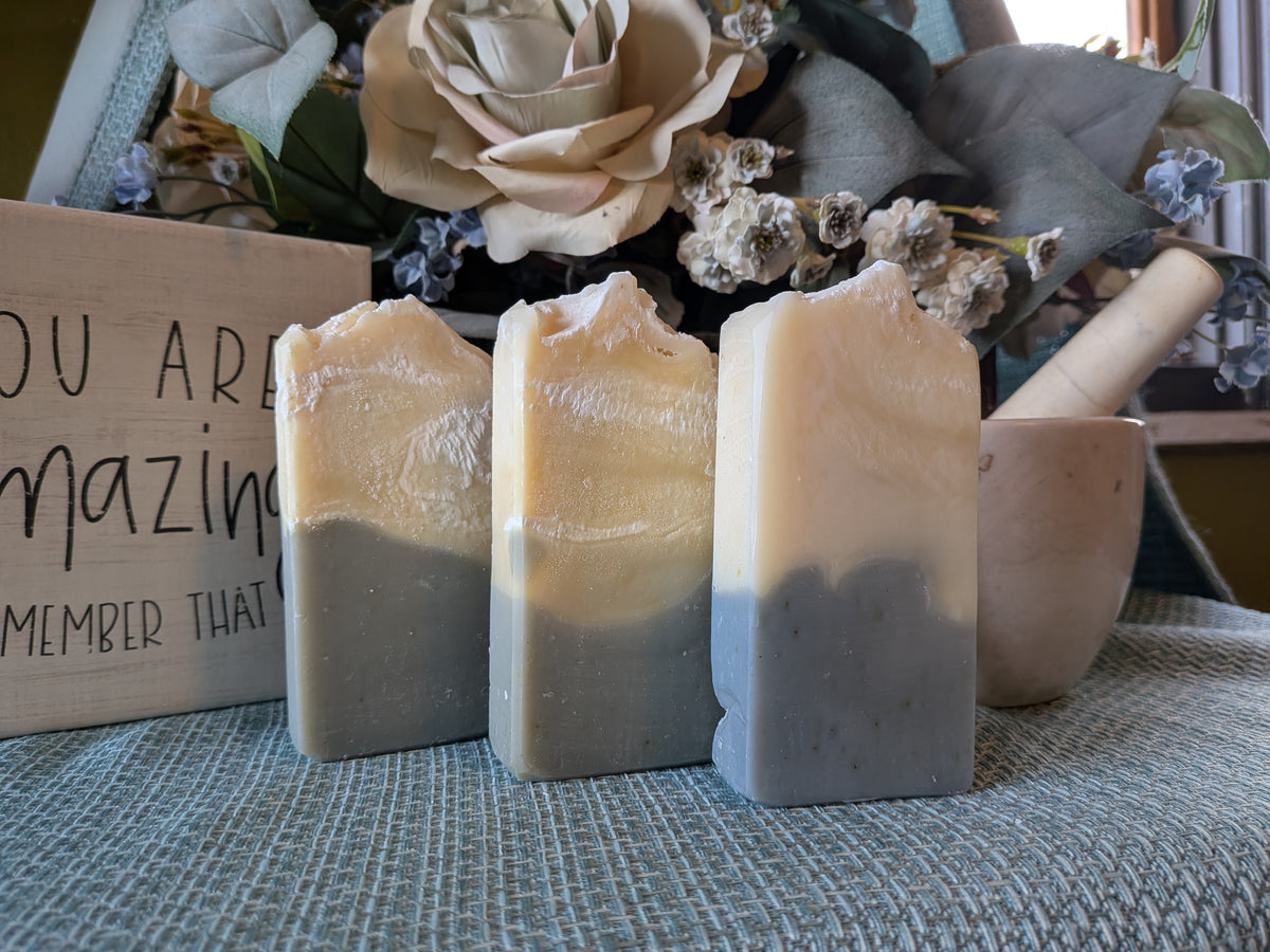 Three upright bars of Just Breathe 100% Tallow Soap displayed side-by-side on a blue textured surface, showing two-toned layers of cream and blue
