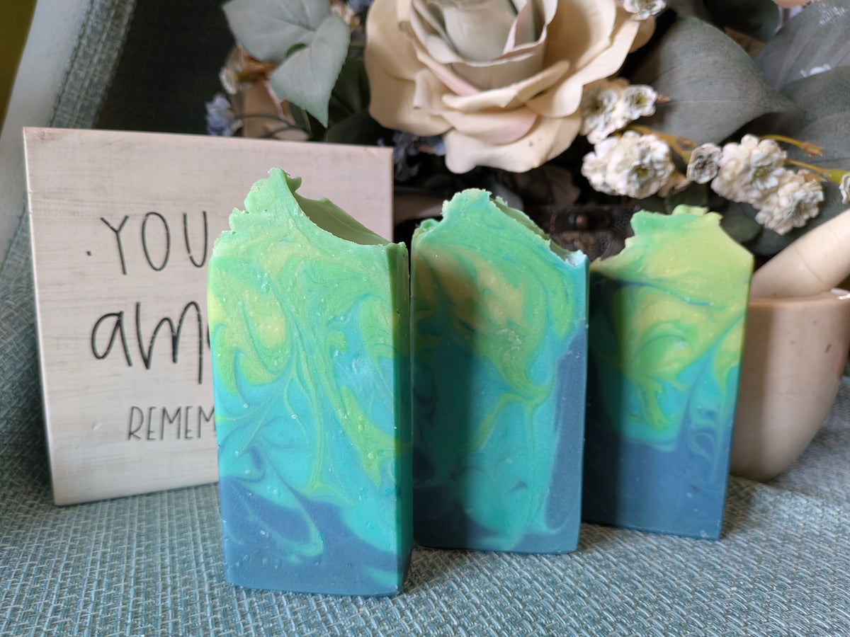 Three marbled blue and green soap bars with a wooden sign in the background.