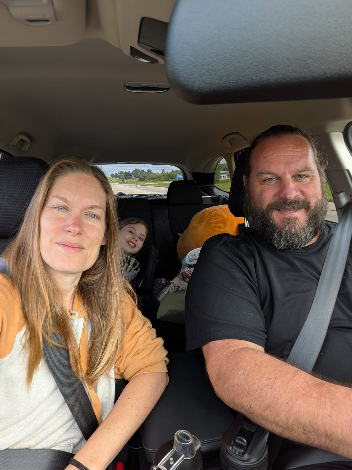 Family of three sitting in a car with a child in the back seat.