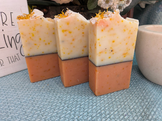 "Three upright bars of Calendula Double Butter Soap displayed side-by-side on a blue textured surface, showing two-toned layers of cream top and terracotta bottom."